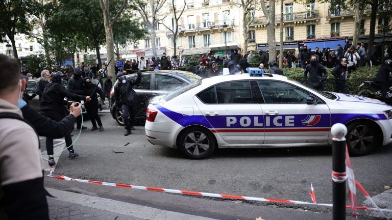 a police officer draws his weapon in Paris while his vehicle is attacked by hooded individuals