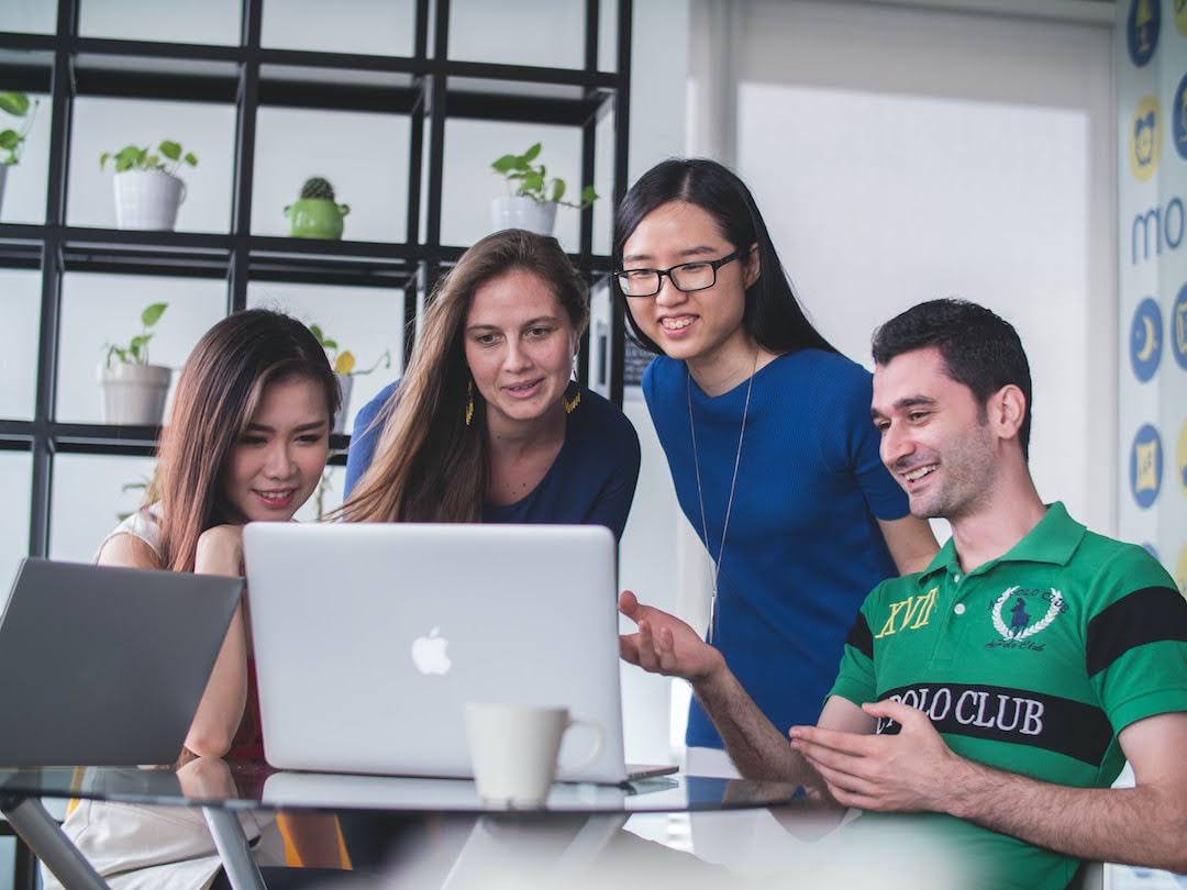 Four people smiling and looking at a laptop, discussing HIPAA fax compliance.