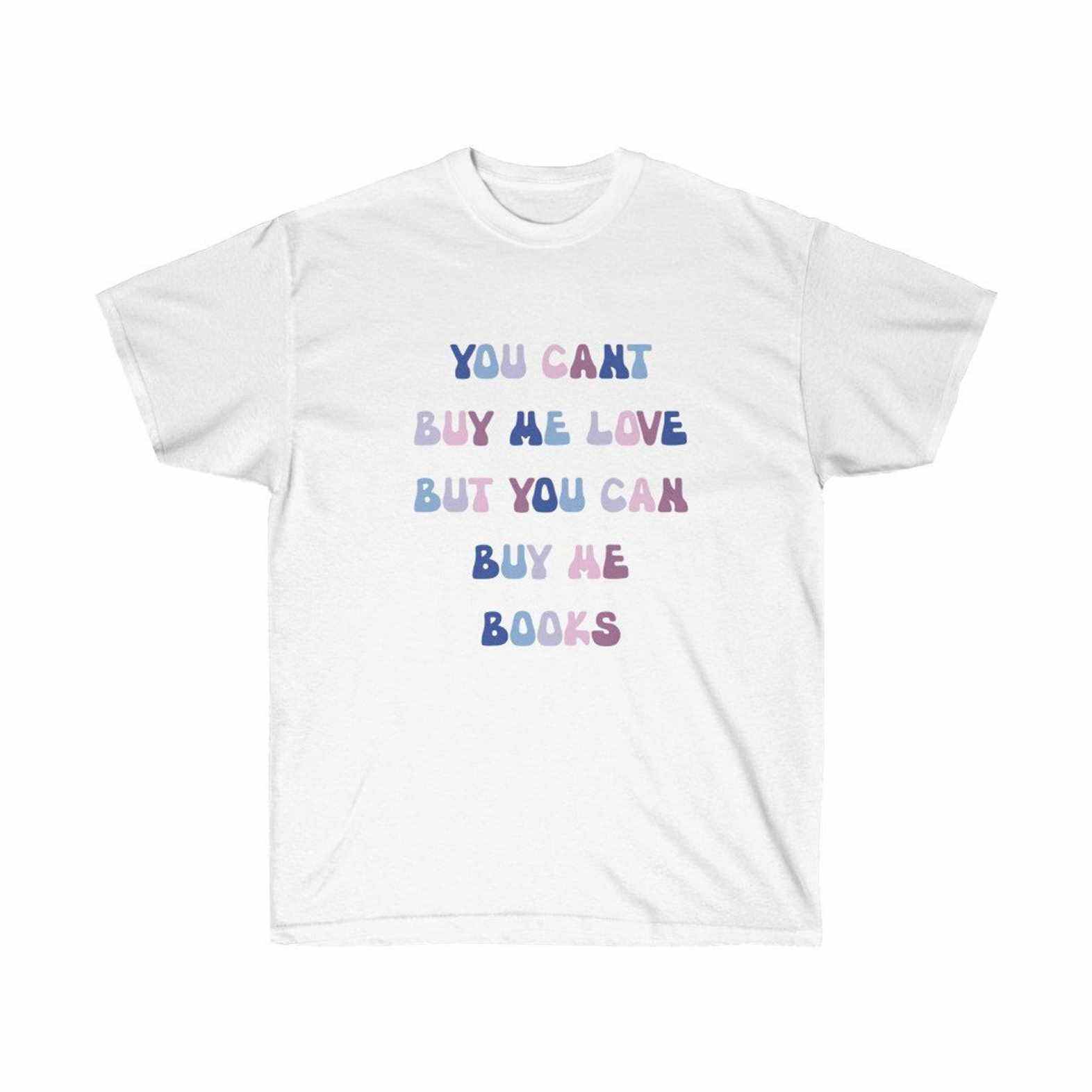 T-shirt blanc avec texte dans une gamme de couleurs rose, violet et bleu.  Le texte lit "tu ne peux pas m'acheter de l'amour mais tu peux m'acheter des livres." 