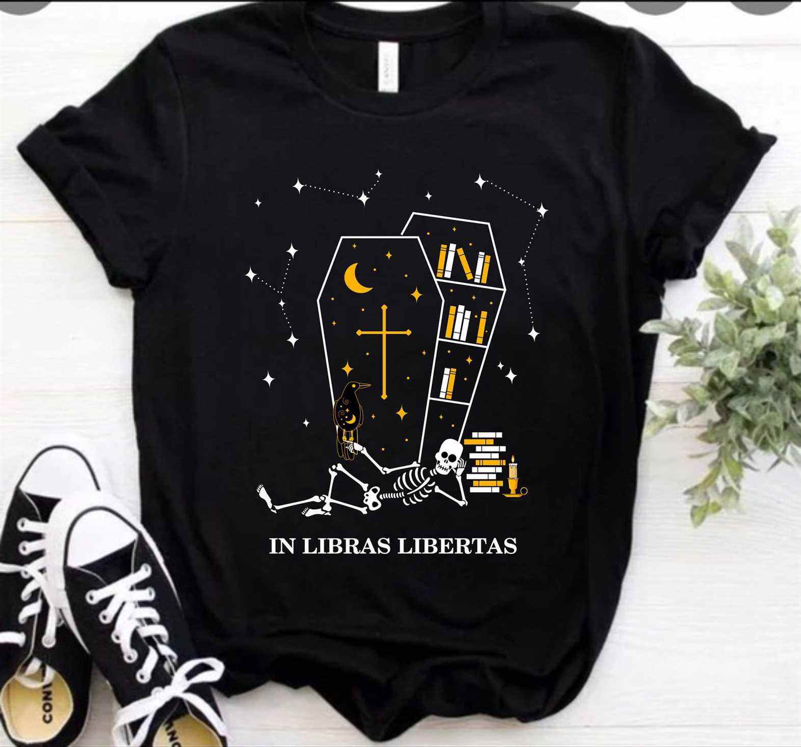 Image d'un t-shirt noir.  Il y a un cercueil rempli de livres dessus, et un squelette allongé devant.  Ça lit "dans libras libertas." 