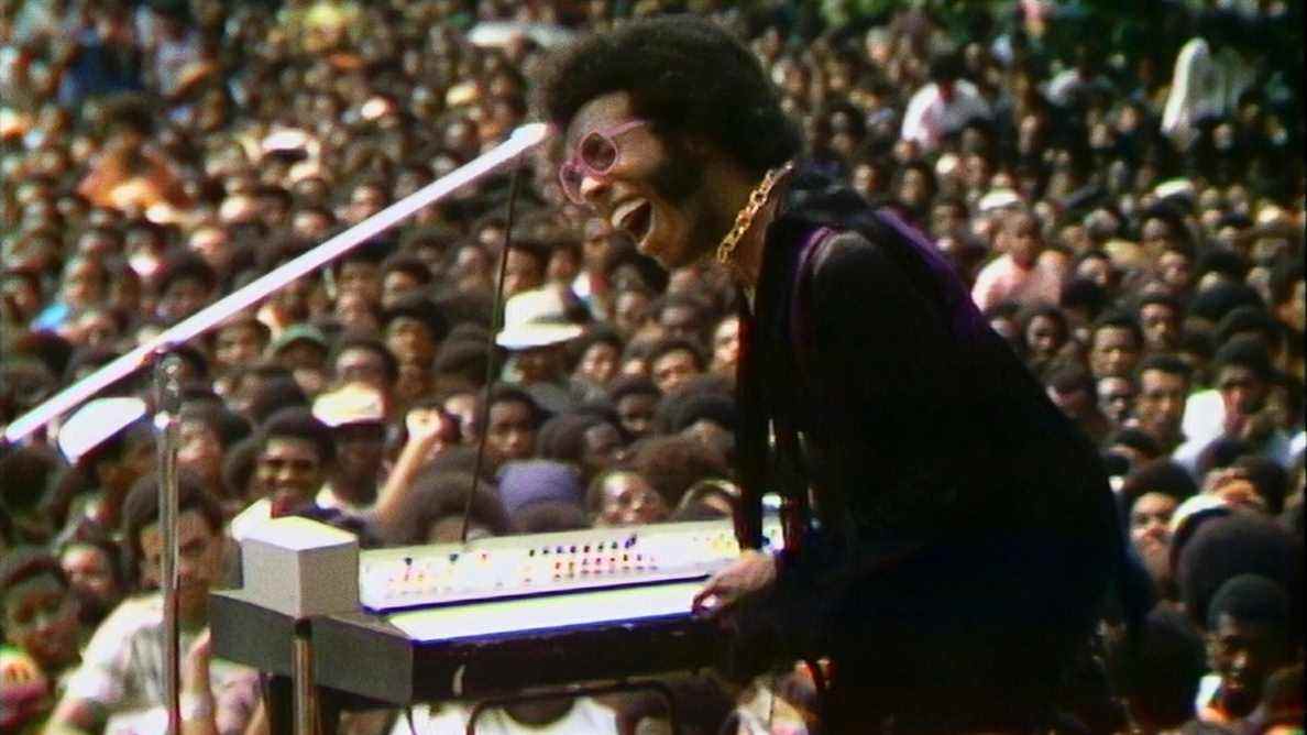 Sly Stone en performance avec une foule immense en arrière-plan dans Summer of Soul