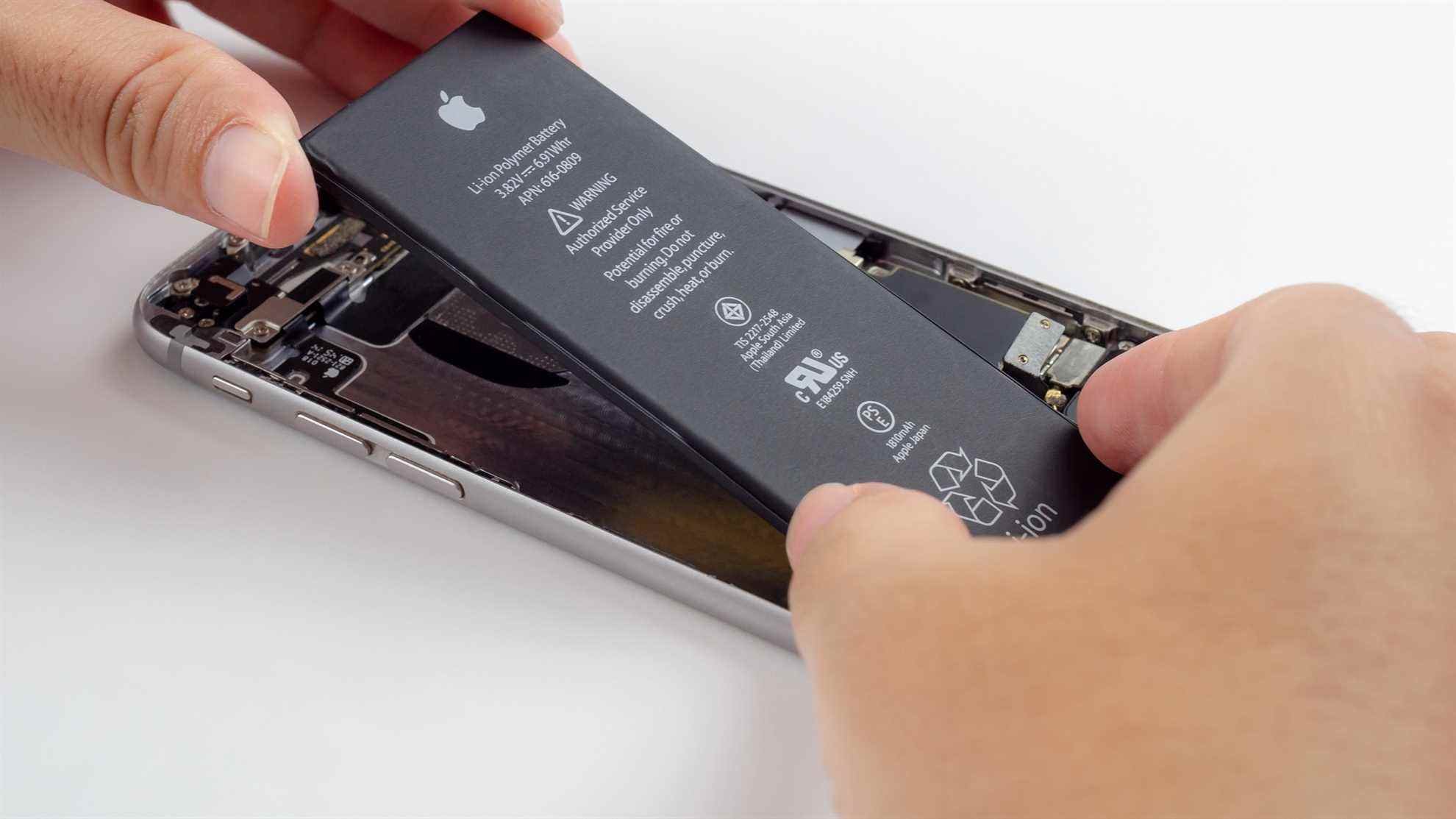 Image en gros plan des mains d'un technicien essayant de retirer, de retirer, de changer ou de remplacer la batterie d'Apple iPhone 6 dégénérée ou endommagée.