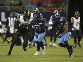 Hamilton Tiger Cats, Steven Dunbar Jr. WR (82) est sur le point d'être abordé par Toronto Argos Henoc Muamba LB (10) et son coéquipier Crezdon Butler DB (24) lors du match du 12 novembre à Toronto.  Les Argos l'ont remporté pour décrocher la première place du classement de la division Est de la LCF.