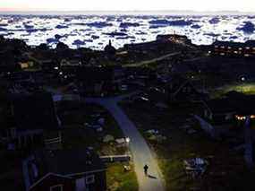 Un piéton marche au crépuscule alors que la glace et les icebergs flottent dans la baie de Disko le 2 septembre 2021 à Ilulissat, au Groenland.