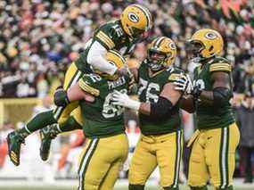 Le quart-arrière des Green Bay Packers Aaron Rodgers (12) est relevé par le gardien Lucas Patrick (62) après avoir établi le record de franchise pour le plus de touchés par la passe au premier quart lors du match contre les Browns de Cleveland au Lambeau Field.