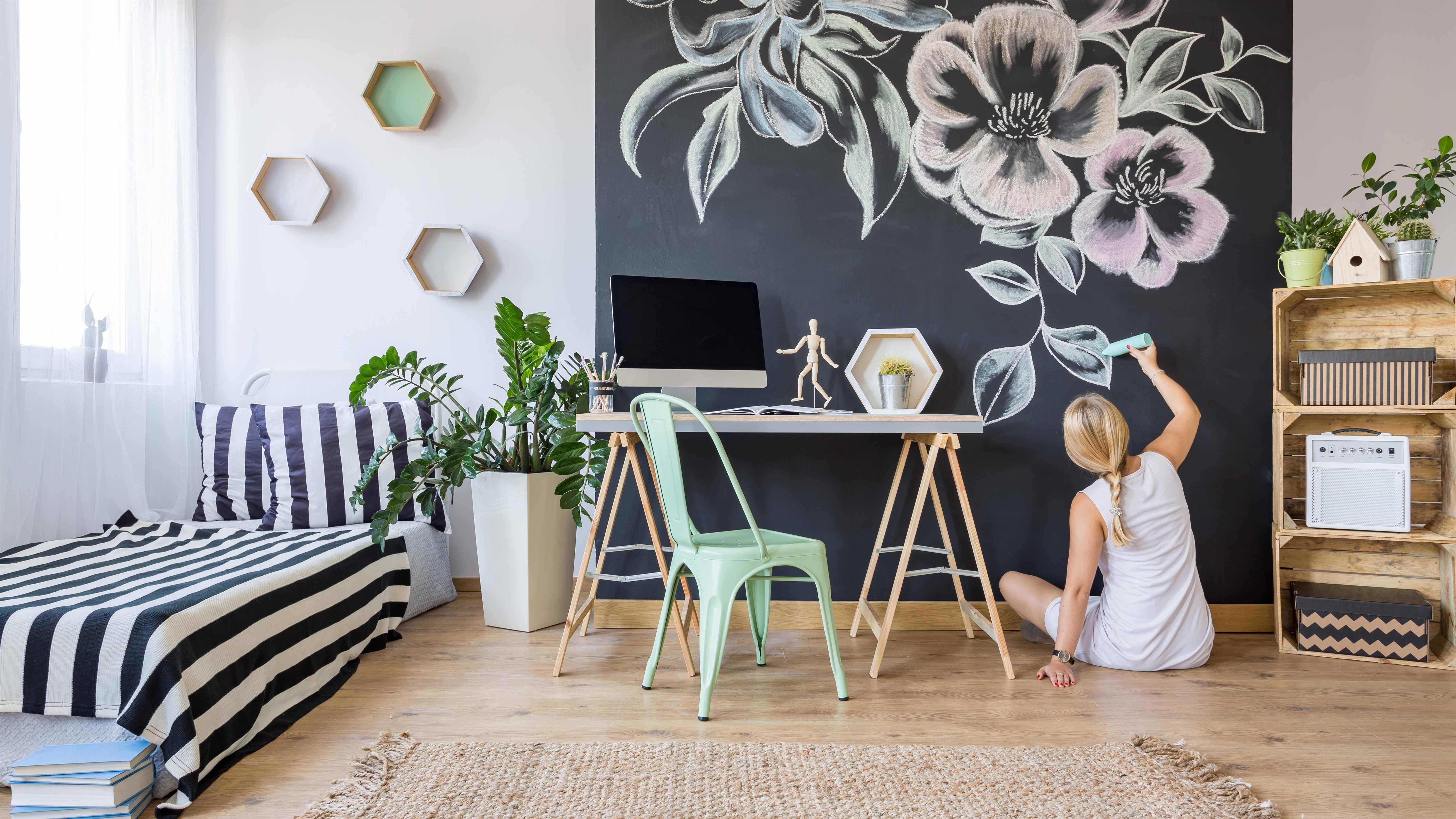 Une femme dessinant un motif de fleurs sur un tableau derrière son bureau