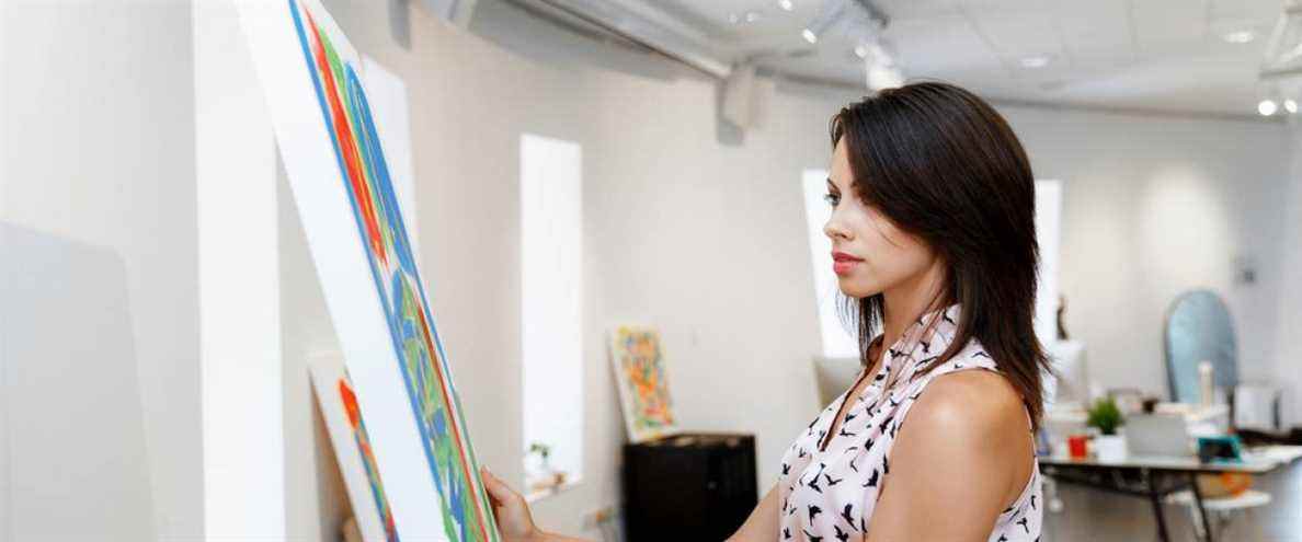 Jeune femme caucasienne debout dans une galerie d'art devant la peinture affichée sur un mur blanc