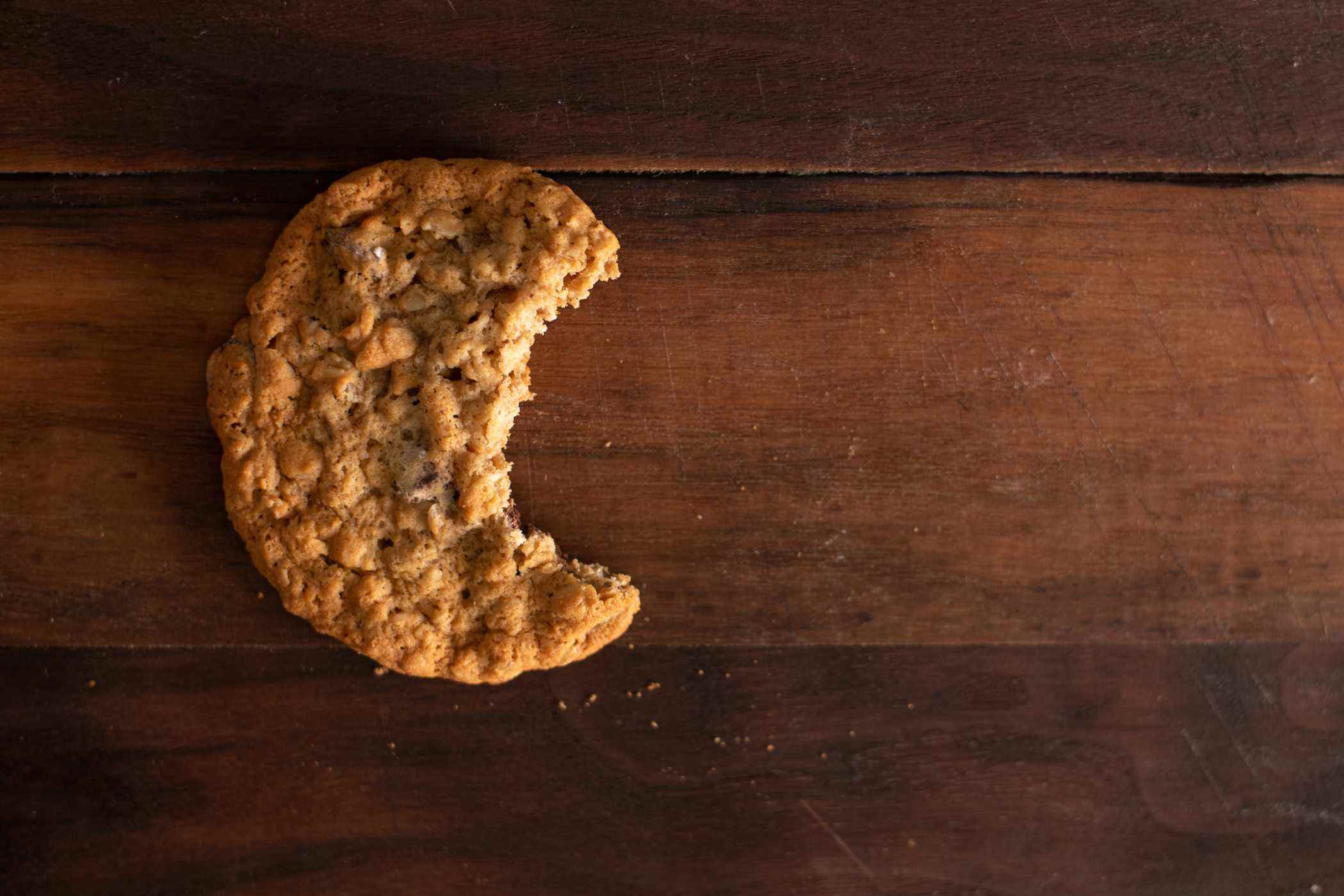 Un biscuit aux pépites de chocolat à l'avoine avec une bouchée sur une planche en bois de noyer.