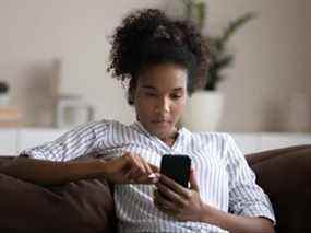 Femme afro-américaine ciblée utilisant un smartphone, assise sur un canapé