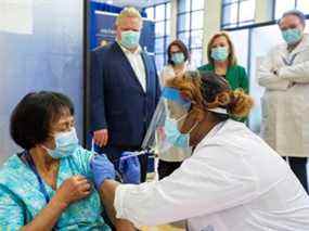 Le premier ministre Doug Ford et la ministre de la Santé Christine Elliott regardent un travailleur de la santé administrer la deuxième dose du vaccin Pfizer-BioNTech à la préposée aux services de soutien à la personne Anita Quidangen, qui est la première personne en Ontario à recevoir les deux doses, le 4 janvier 2021.