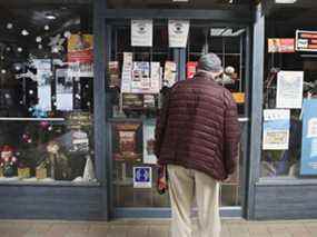 Un piéton vérifie les heures d'ouverture d'un magasin de magazines à Montréal qui a été fermé dimanche en raison de restrictions visant à freiner les hospitalisations pour coronavirus.