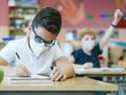 Un élève dans une salle de classe assis à un bureau avec un masque de protection le premier jour d'école, écrit dans son cahier.