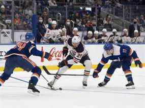 Le centre des Oilers d'Edmonton Leon Draisaitl (29) patine avec la rondelle alors que le défenseur des Islanders de New York Scott Mayfield (24) et l'ailier gauche Matt Martin (17) défendent au cours de la première période à l'UBS Arena le janv.  1, 2022.