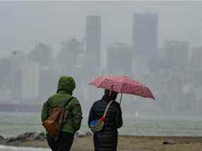 Des marcheurs marchent sous la pluie le long des banques espagnoles alors que la ville est cachée derrière un mur de pluie à Vancouver, le 7 novembre 2021.