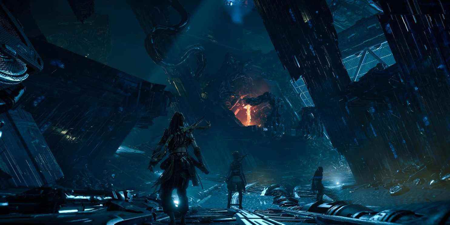 aloy debout dans une grande structure métallique avec des piliers inclinés soutenant le toit et un bras métallique versant de la lave dans une fosse au loin