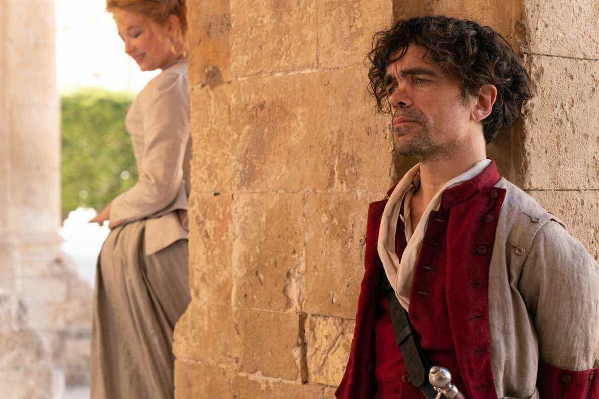 Haley Bennett dans le rôle de Roxanne sourit de l'autre côté d'un pilier de pierre de Peter Dinklage dans le rôle de Cyrano dans Cyrano de Joe Wright