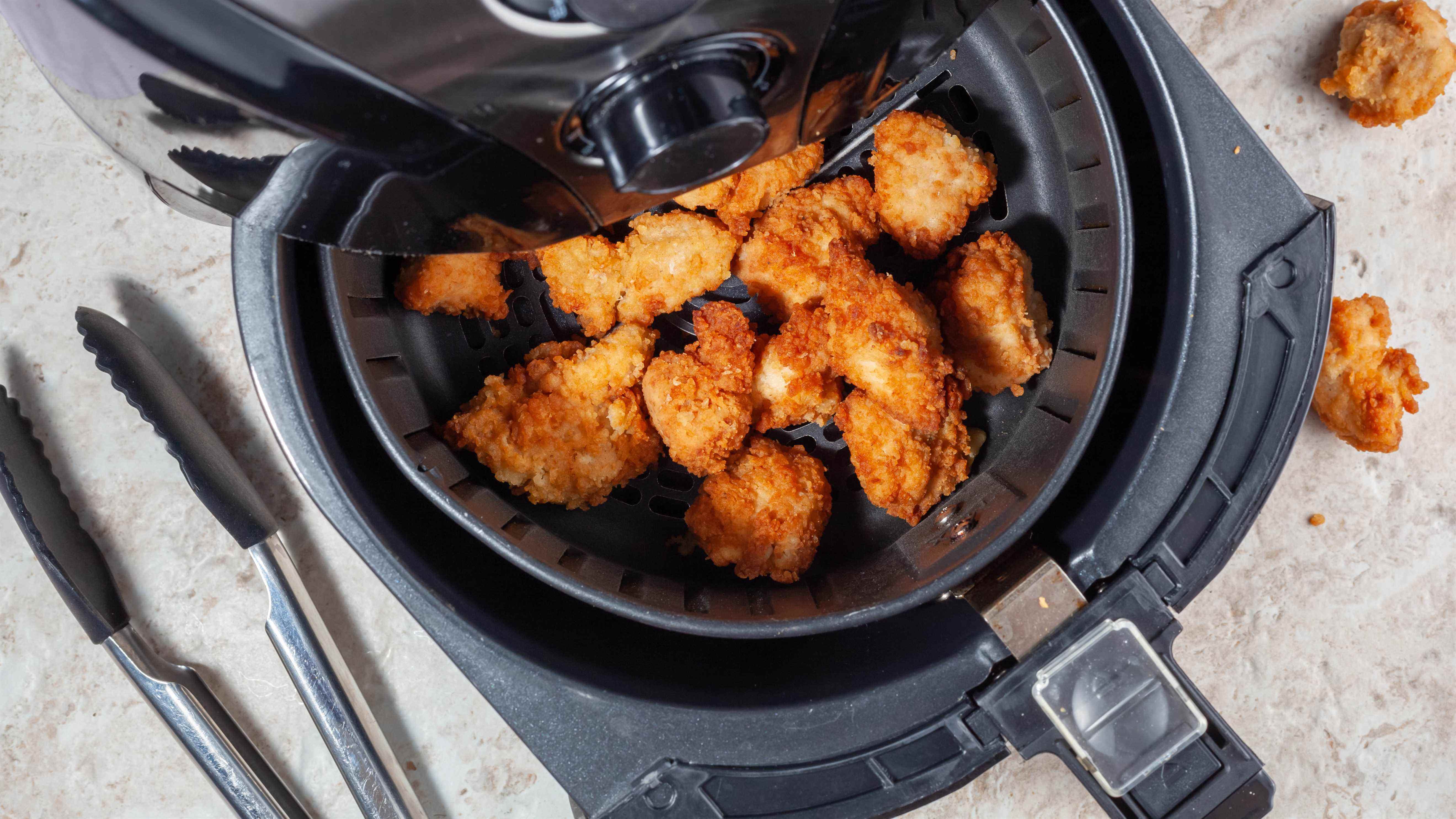 Une friteuse à air avec des pépites de poulet disposées uniformément sur le panier