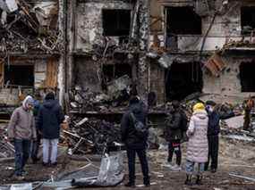 Les gens regardent l'extérieur d'un bloc résidentiel endommagé touché par une frappe de missile tôt le matin le 25 février 2022 à Kiev, en Ukraine.