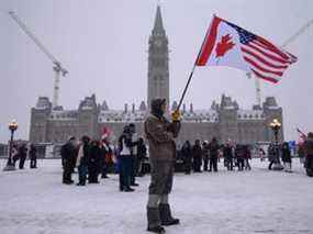 Un manifestant tient un drapeau américain et canadien lors d'une manifestation de camionneurs contre les mandats de la COVID-19, devant le Parlement du Canada à Ottawa le 12 février 2022.