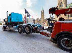 Un camion est remorqué devant la colline du Parlement alors que la police s'efforce de rétablir la normalité dans la capitale après que des camions et des manifestants ont occupé le centre-ville pendant plus de trois semaines pour protester contre les restrictions liées à la pandémie.