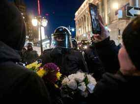 Une femme diffuse en direct tout en distribuant des fleurs devant la police alors que les manifestants se rassemblent et font la fête sur la rue Kent après que la police a dégagé la rue Wellington, précédemment occupée par le Freedom Convoy, à Ottawa, le 19 février 2022.