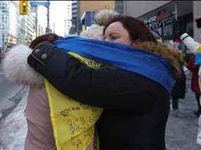 Tatiana Lipman, à droite, une manifestante canado-ukrainienne embrasse et enroule un drapeau autour de son amie devant le consulat russe sur St. Clair Ave. E. juste à l'est de Yonge St. expriment leur mécontentement envers le dirigeant russe Vladimir Poutine et son invasion à grande échelle avec les forces russes attaquant l'Ukraine le jeudi 24 février 2022.