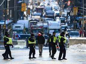 Un manifestant transportant un bidon de carburant vide sur un manche à balai passe devant des agents de la Police provinciale de l'Ontario, en signe de protestation contre les restrictions liées à la COVID-19 qui ont été marquées par des embouteillages et le son des klaxons des camions se poursuit dans sa deuxième semaine à Ottawa le lundi 21 février. 7, 2022. LA PRESSE CANADIENNE/Justin Tang