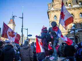 Un manifestant se tient debout sur la statue de Terry Fox à laquelle a été ajouté un drapeau du Canada à l'envers.