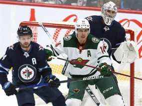 Le centre du Wild du Minnesota Joel Eriksson Ek (au centre) écarte le défenseur des Jets de Winnipeg Josh Morrissey alors qu'il s'installe devant le gardien de but Connor Hellebuyck à Winnipeg le mercredi 16 février 2022.