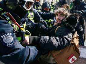 Un agent portant un insigne de la Police d'Ottawa arrête un manifestant lors d'une manifestation menée par des camionneurs devant le Parlement du Canada à Ottawa le 18 février 2022.