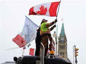 Des gens agitent des drapeaux au sommet d'un camion devant la colline du Parlement alors que les camionneurs et leurs partisans continuent de protester contre les mandats de vaccination contre la COVID-19 à Ottawa, Ontario, Canada, le 6 février 2022.