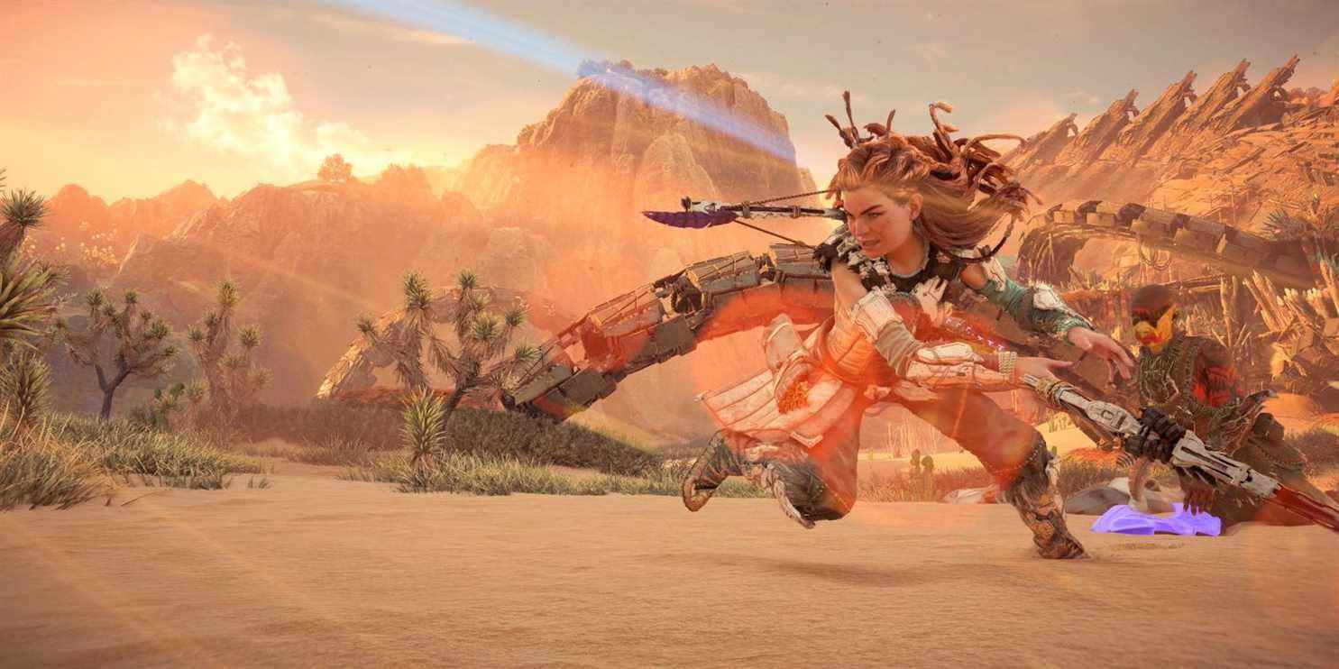 aloy debout dans un désert balançant sa lance dans un grand arc tandis qu'un soldat ennemi s'agenouille sur le sol derrière elle