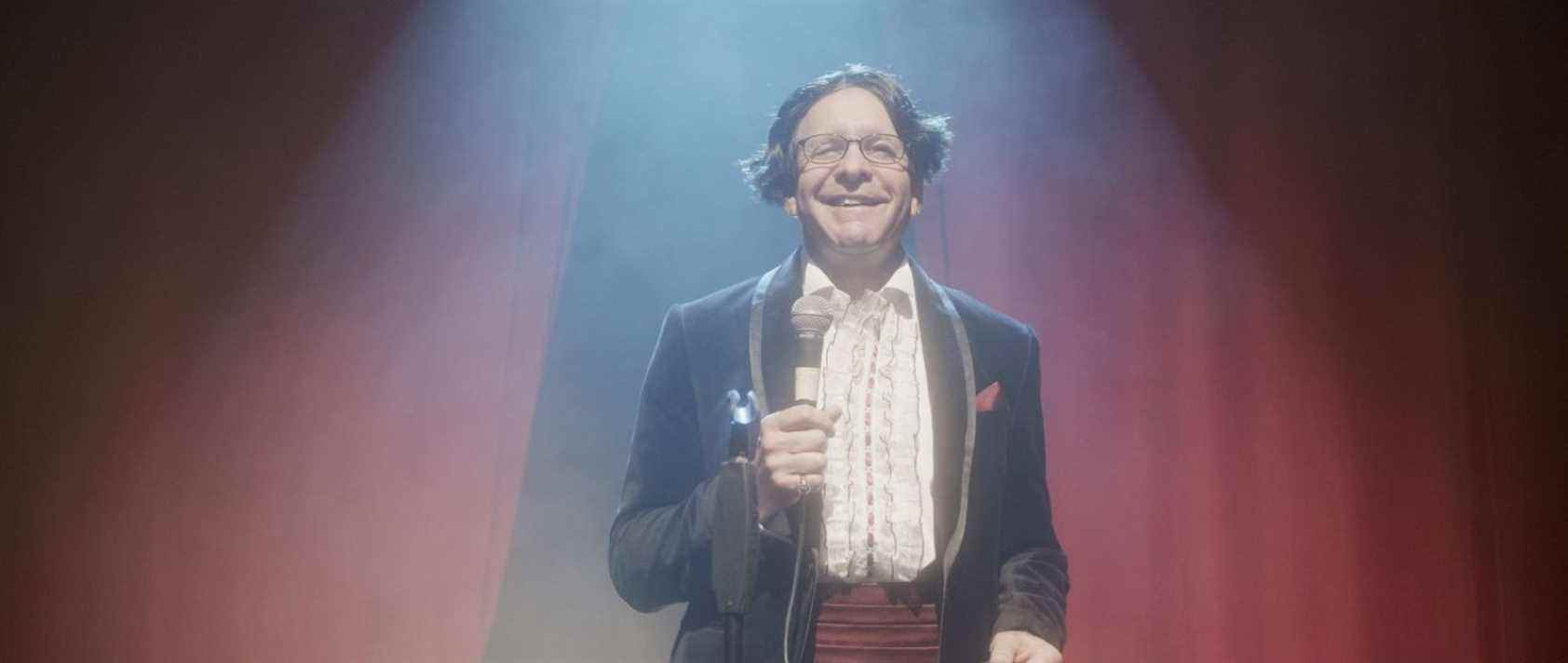 Steve Guttenberg on stage with a bad wig and tux doing stand up