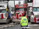 Un policier monte la garde près de camions participant à un blocus des rues du centre-ville près des édifices du Parlement à Ottawa le 16 février 2022.