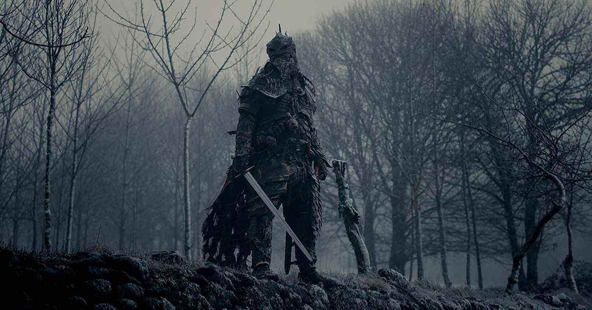 Un guerrier en armure noire se tient devant une forêt d'hiver désolée.