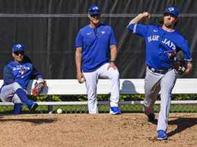 Le gérant des Blue Jays Charlie Montoyo (à gauche) et l'entraîneur des lanceurs Pete Walker (au centre) regardent le lanceur partant Kevin Gausman lancer dans l'enclos des releveurs lors d'un entraînement printanier.