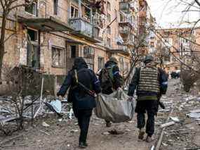 La police ukrainienne transporte un corps loin d'un immeuble résidentiel de cinq étages qui s'est partiellement effondré après un bombardement à Kiev le 18 mars 2022.