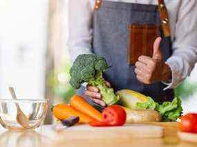 Une femme chef tenant et faisant le pouce vers le haut pour montrer bon signe à un brocoli vert avec un plateau de légumes