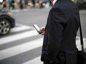 Un piéton regarde un smartphone alors qu'il se tient à un coin du quartier financier de Toronto.