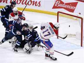 Josh Anderson des Canadiens marque sur le gardien des Jets Connor Hellebuyck alors que Dylan DeMelo défend mardi soir à Winnipeg.  Anderson a réussi son premier tour du chapeau en carrière dans la défaite 8-4 de son équipe.