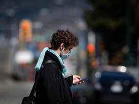 Un homme portant un masque protecteur regarde son téléphone en marchant dans le Downtown Eastside de Vancouver.