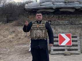 Le père Yuriy, un citoyen canadien qui était retourné temporairement dans son Ukraine natale, devant un poste de contrôle renforcé dans l'ouest de l'Ukraine.  Le prêtre ukrainien-catholique a déclaré que lui et sa femme restaient sur place et qu'il avait rejoint la Force de défense territoriale du pays.  Il a demandé que son nom de famille ne soit pas publié pour des raisons de sécurité.  Crédit : fourni