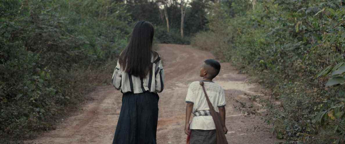 Un jeune garçon lao et son compagnon fantôme marchent le long d'un chemin de terre à travers la forêt dans The Long Walk de Mattie Do