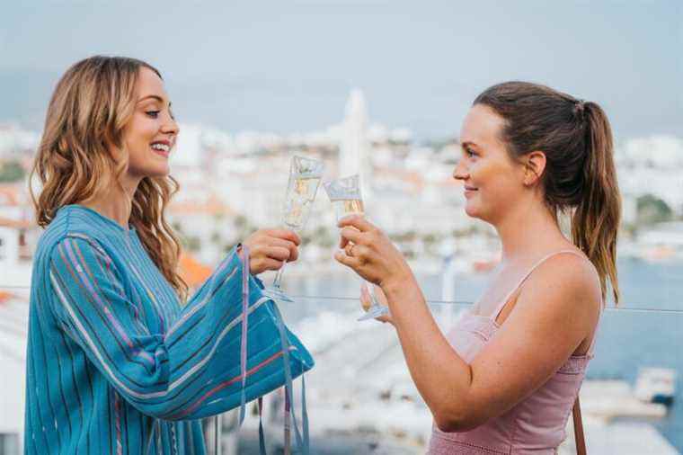 Two women clink champagne glasses on European balcony.