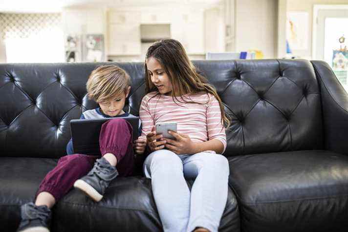 Enfants utilisant des appareils intelligents sur un canapé à la maison ;