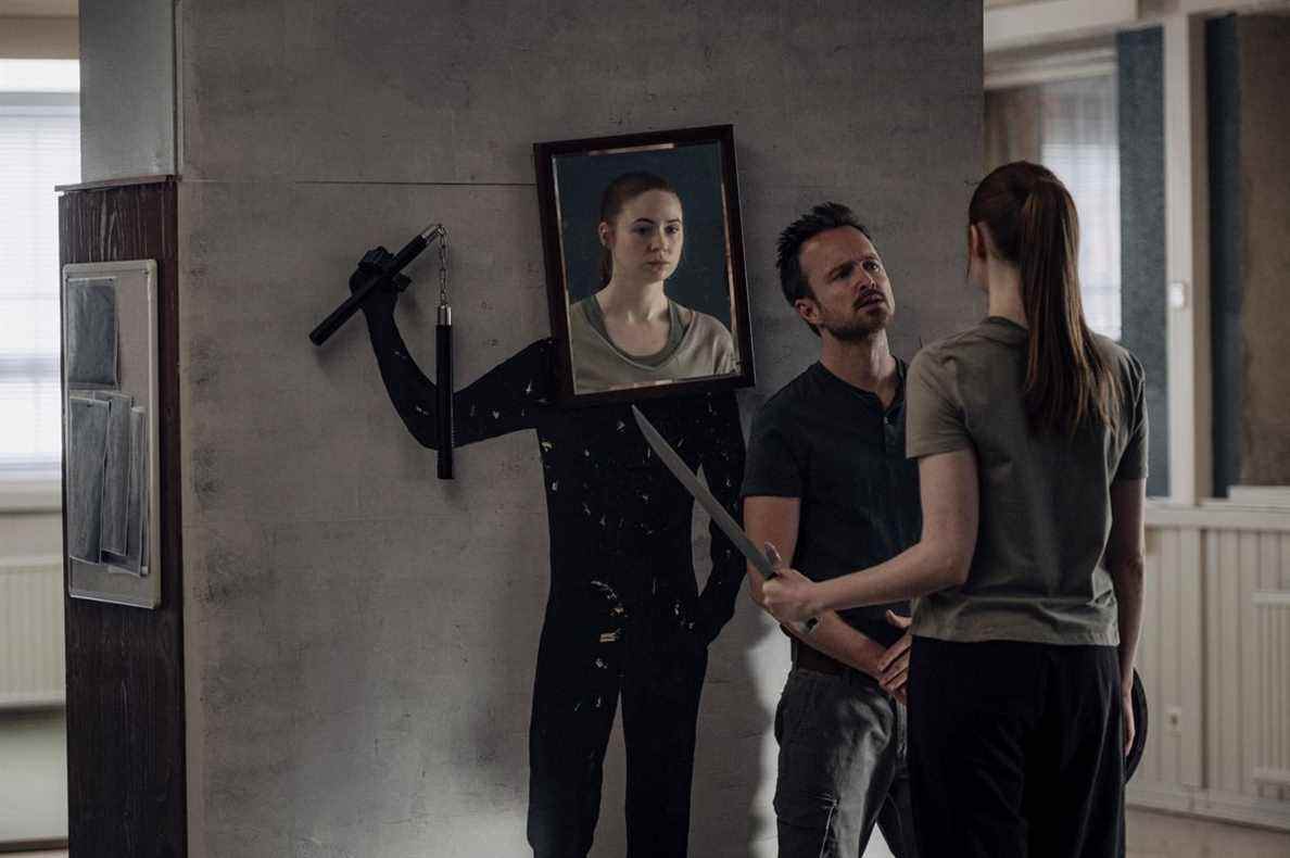 Aaron Paul a Karen Gillan, brandissant un katana, face à une découpe avec une photo de son visage attachée, brandissant des nunchucks, dans Dual