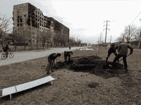 Des gens creusent une tombe pour les victimes tuées pendant le conflit entre l'Ukraine et la Russie dans une rue de la ville portuaire assiégée de Marioupol, en Ukraine, le 20 mars 2022.