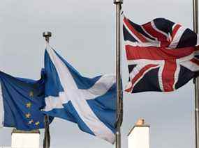 Un sautoir écossais (C) vole entre un drapeau de l'Union (R) et un drapeau de l'Union européenne (UE), devant le bâtiment du Parlement écossais à Édimbourg.