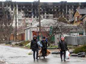 Des résidents locaux marchent devant un immeuble résidentiel endommagé au cours du conflit entre l'Ukraine et la Russie, un jour de pluie dans la ville portuaire du sud de Marioupol, en Ukraine, le 13 avril 2022.