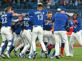 Les joueurs des Blue Jays de Toronto entourent le voltigeur gauche Raimel Tapia alors qu'ils célèbrent sa mouche sacrificielle qui a marqué le point gagnant contre les Red Sox de Boston lors de la 10e manche au Rogers Center le 26 avril 2022.